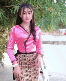 a woman wearing a pink top and a skirt stands in front of a bamboo tree