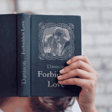 a person covering their face with the book forbidden love