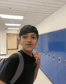 a boy stands in a hallway with blue lockers and a red exit sign