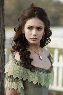 a woman wearing a green dress and a necklace stands in front of a white picket fence