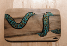 a painting of a snake on a wooden cutting board with the name mcderm on the bottom