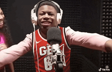 a man wearing headphones and a red jersey with the number 6 on it stands in front of a microphone