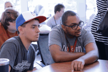 a man wearing a gray shirt that says ' tmc ' on it sits at a table