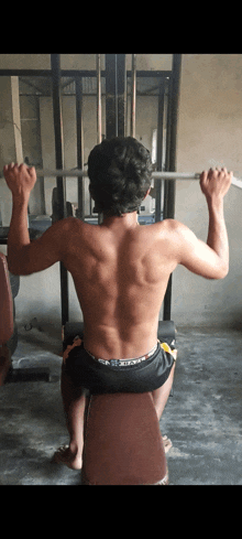 a shirtless man sits on a bench holding a barbell