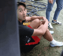 a man sits on the grass with his legs crossed wearing a black shirt that says ' soccer ' on it