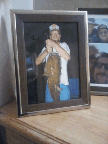 a framed picture of a man holding a large fish with a hat that says ' duke ' on it