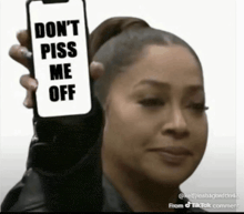 a woman is holding up a cell phone that says `` don t piss me off '' .