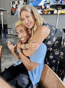 a woman in a floral dress is hugging a smiling man in a blue shirt