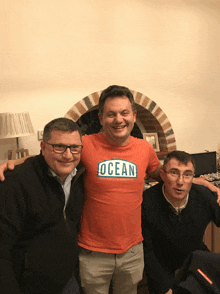 three men are posing for a picture with one wearing an orange shirt that says ocean