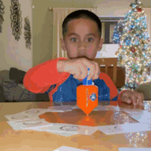 a young boy is playing with an orange toy with the number 3 on it in front of a christmas tree