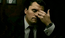 a man in a suit and tie has his hand on his face