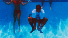 a man is squatting in a swimming pool with two women swimming in the background