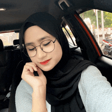 a woman wearing glasses and a black hijab is sitting in a car