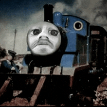 a blue train with a face painted on it is sitting on the tracks .