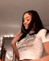 a woman wearing a white crop top and hoop earrings is standing in a room .