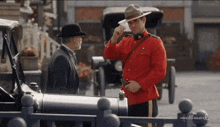 a man in a red uniform is talking to another man in a black hat in front of a hallmark sign