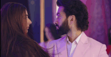 a man with a beard in a pink suit looks at a woman