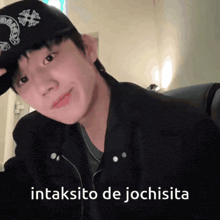 a young man wearing a black hat and a black jacket says " intaksito de jochisita " on the bottom