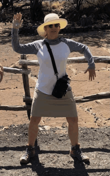 a woman wearing a hat and sunglasses is standing in front of a fence