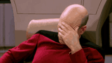 a bald man in a red shirt is covering his face