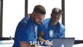 two men in blue scrubs are looking at a laptop computer .