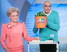 a man is holding a bucket of cucumbers and a woman is standing next to him