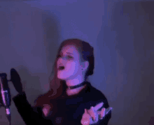 a woman is singing into a microphone in a dark room with purple lights behind her .