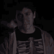 a man wearing a skeleton shirt and a hoodie is standing in the dark .