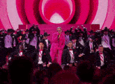 a man in a pink suit is singing into a microphone surrounded by men in tuxedos