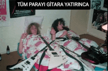 two people are laying on a bed with guitars around them and a sign that says tüm parayi gitara yatirinca