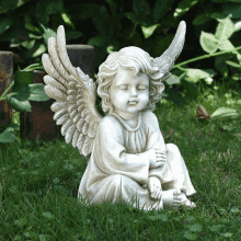 a statue of an angel sitting on the grass with his eyes closed