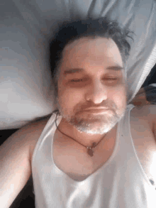 a man with a beard wearing a white tank top is laying on a bed