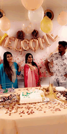 a group of people standing around a table with balloons and a sign that says welcome