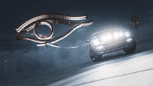 a car is driving down a road at night with a statue of an eye in the background