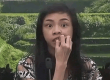 a woman is biting her nails in front of a microphone and making a funny face .