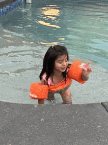 a little girl is swimming in a pool wearing a life preserver that says swim academy