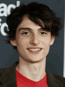 a young man wearing a red shirt and a brown jacket smiles for a picture