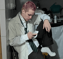 a man with pink hair is leaning against a wall while looking at his phone