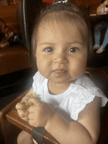 a baby girl is sitting in a high chair holding a green plant in her hand