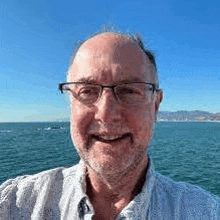 a man wearing glasses is smiling in front of a body of water .