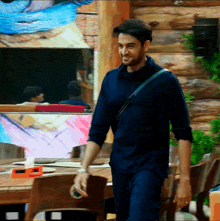 a man in a blue shirt is walking in a room with a painting on the wall behind him