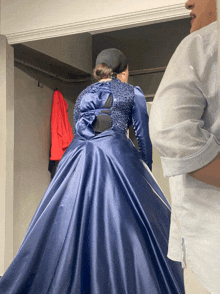 a woman in a long blue dress is standing in a closet