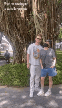 a man and a woman standing in front of a tree with a caption that says when mom asks you to stand for a photo