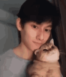 a young man is holding a cat in his arms and looking at the camera .