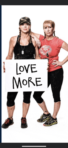 two women holding a sign that says " love more "