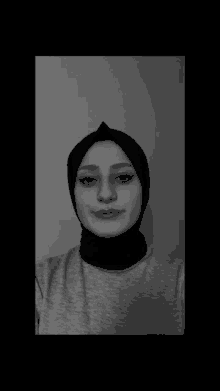 a black and white photo of a woman wearing a hijab and a grey shirt .