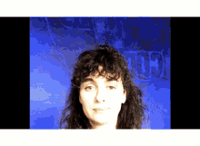 a woman with curly hair stands in front of a blue wall with the letters g and h written on it