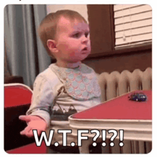 a baby is sitting at a table with a toy car on it and says w.t.f.