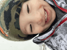 a young boy wearing a camouflage hat and a jacket smiles in the snow