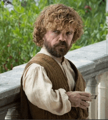 a man with curly hair and a beard is leaning on a railing holding a cup of coffee